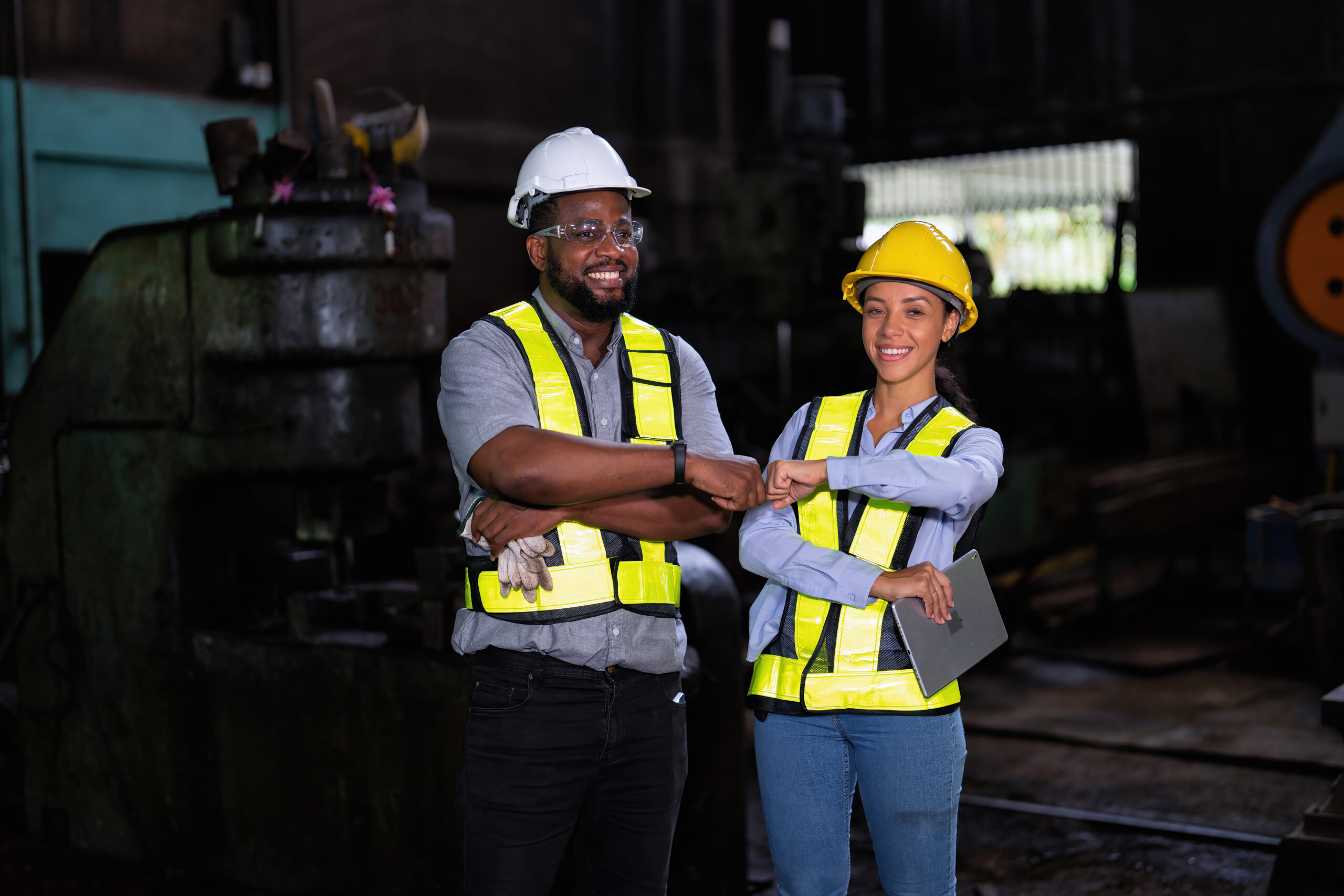 Female worker and coworker posing confidently while standing with arms crossed in factory workshop